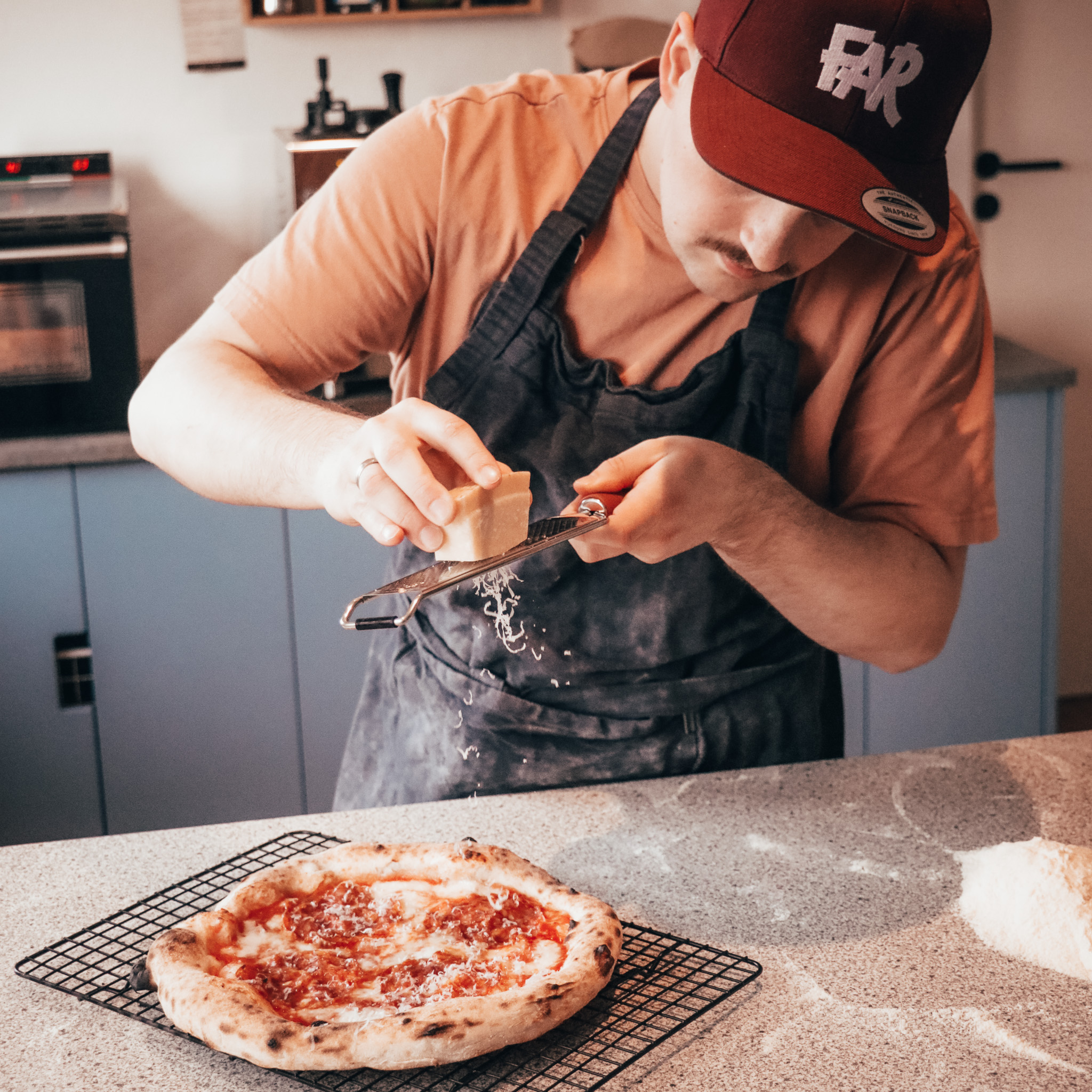 Nørdefar river parmesan over færdig pizza